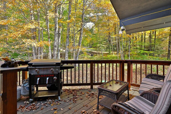 A wooden deck with a grill, wicker furniture, and a view of a forest. - Winding Way Chalet 3 Bedroom Home (Killington)