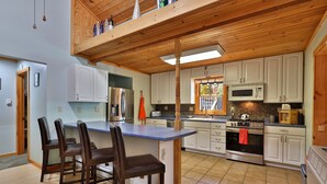 Una cocina moderna con una isla central, armarios blancos, electrodomésticos de acero inoxidable y techo de madera.