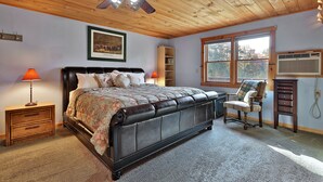 Un dormitorio con una cama grande, techo de madera y ventana con vistas a árboles.