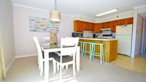 A compact kitchen with wooden cabinets, a central island with stools, a hanging light fixture, and a painting on the wall.