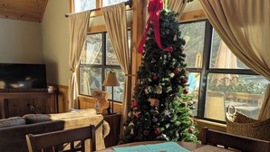 Een eethoek met een houten tafel, stoelen, een kerstboom en een televisie op de achtergrond.