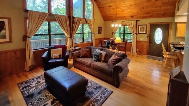 Een gezellig cabin interieur met een houten plafond, grote ramen, een bank, een eettafel en een keukenhoek.