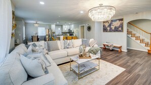 A spacious living room with a large sofa, a coffee table, and a chandelier. A staircase with wooden railings leads to an upper level. - Silver Springs Home: Walk to Downtown! (Silver Spring)