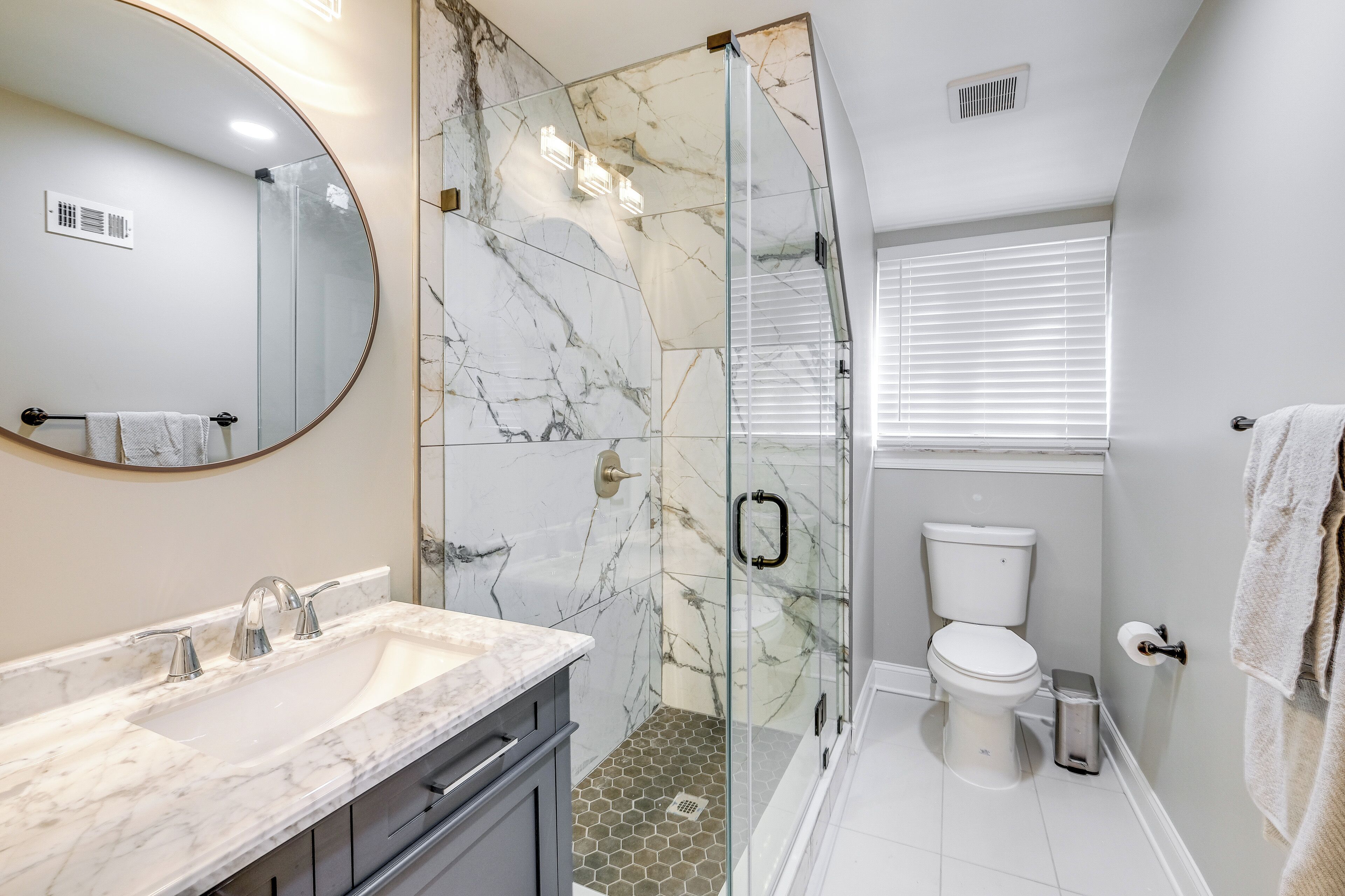 A modern bathroom with a marble sink, a glass shower enclosure, and a toilet.