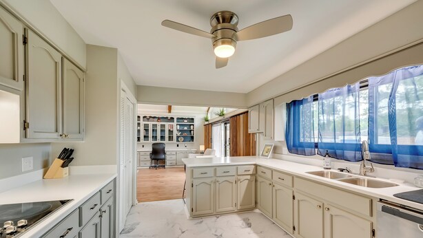 A modern kitchen with a marble floor, white cabinetry, and a ceiling fan.