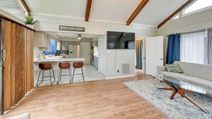 A modern kitchen with wooden cabinets, a central island with stools, and a dining area with a white table and chairs.