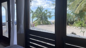Une vue sur la plage depuis un espace abrité, doté d’une rambarde en bois, de palmiers et d’une plage de sable.