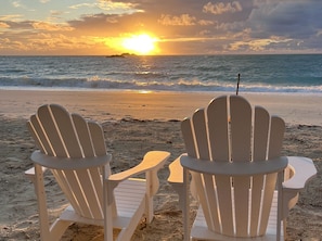 Two white Adirondack chairs facing the ocean with a sunset in the background.