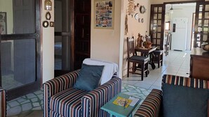Una sala con sofás a rayas, un comedor con sillas de madera y una cocina al fondo.