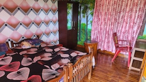 A room with a bed, a wooden chair, a small table, and a wall with a geometric pattern. - Forest home where elephants roam (Seethathode)