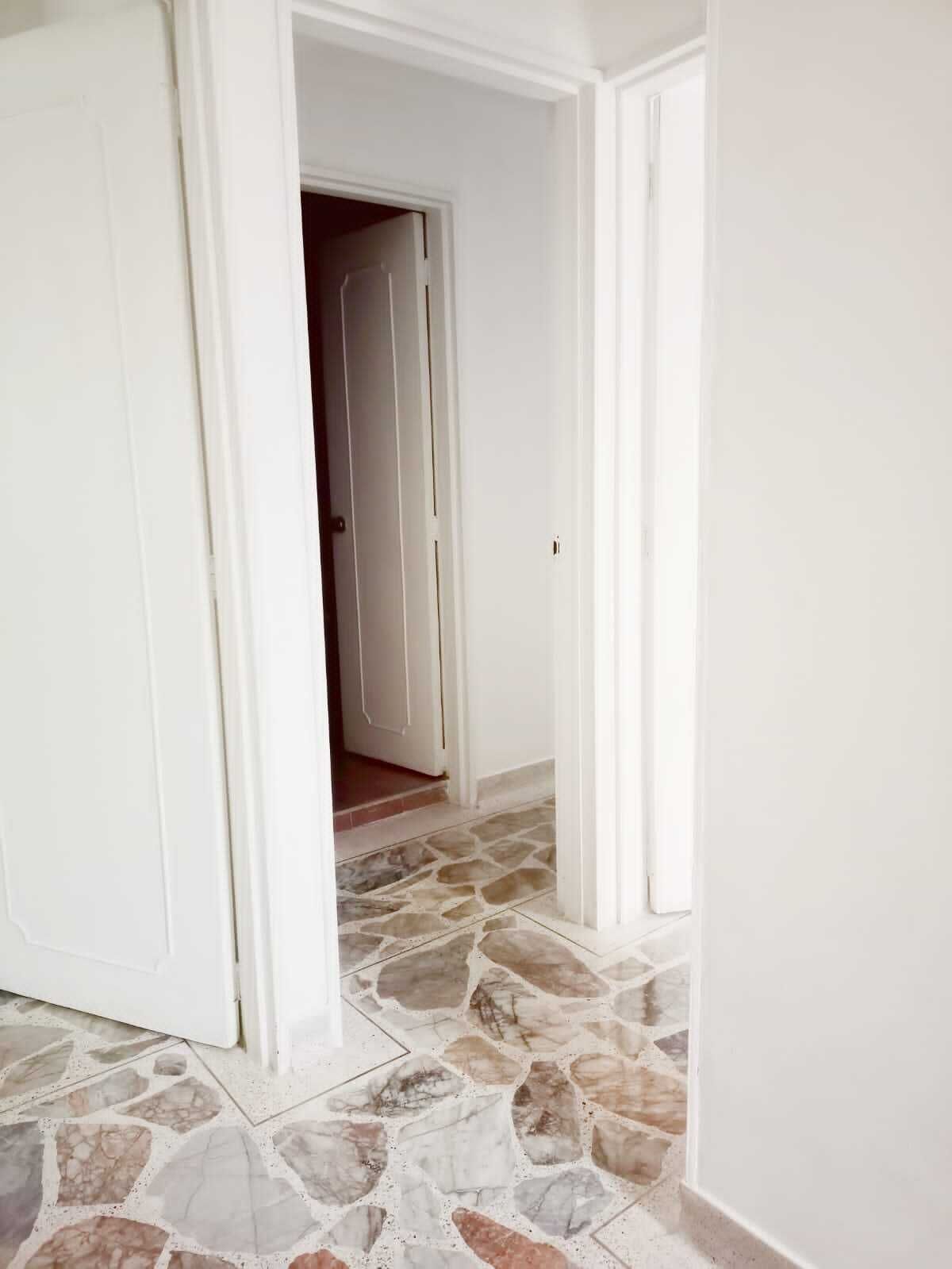 A hallway with white walls and a stone-patterned floor leading to a door.