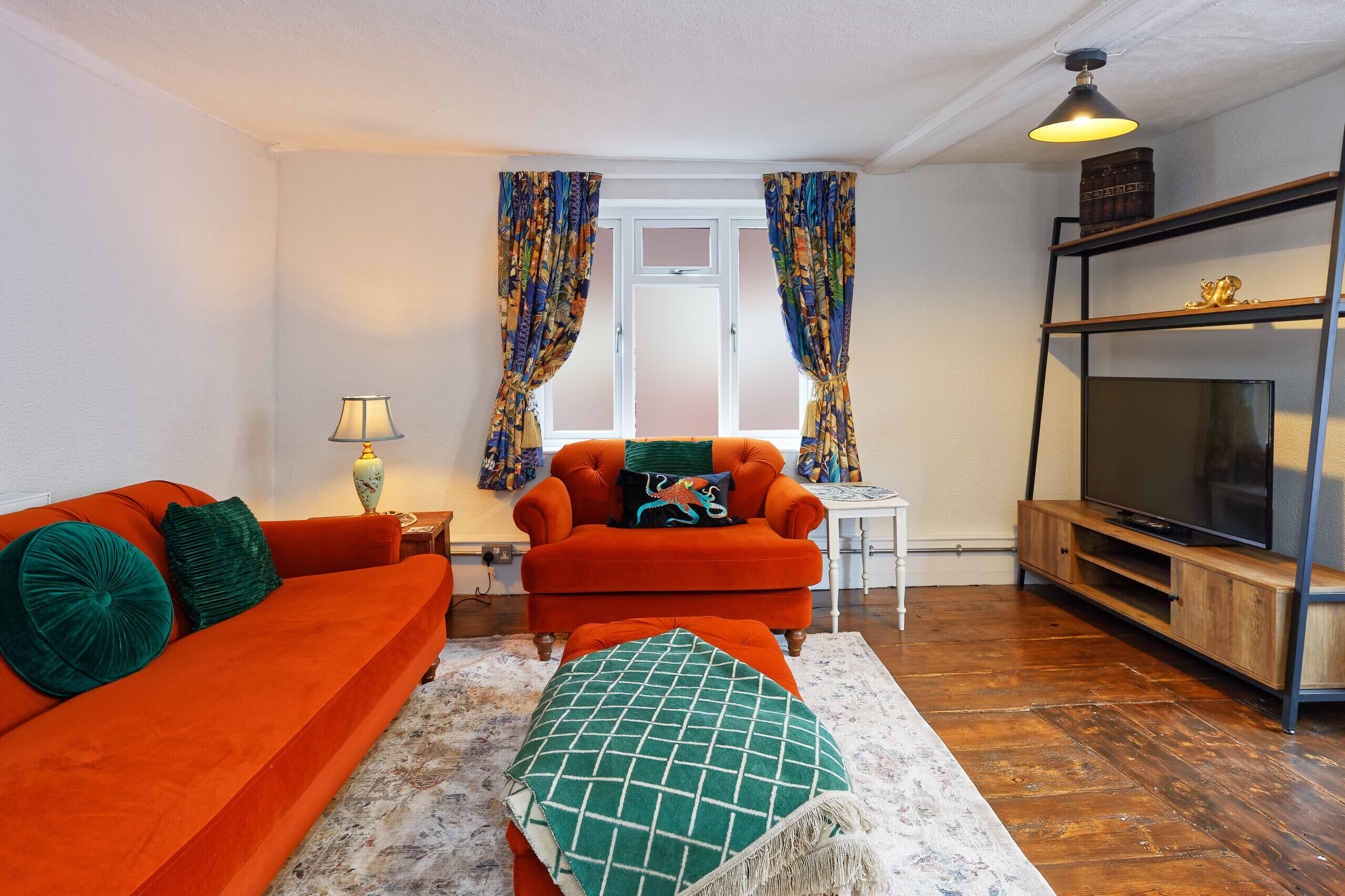 Een woonkamer met een bank, fauteuil, pouf, tv-meubel en gordijnen.
