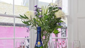Ett dukat bord för en måltid, med en flaska champagne, glas och en vas med blommor.