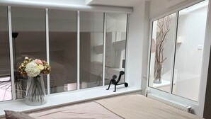 A bedroom with a skylight, a bed, a window with a view, and a vase with flowers.