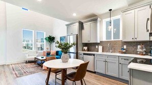 Una cocina moderna con armarios grises, una zona de comedor con una mesa redonda y una sala de estar con un sofá y una planta.