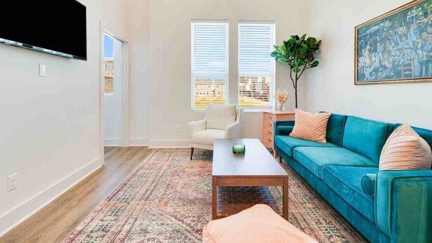 Una sala de estar moderna con un sofá color turquesa, un sillón blanco, una mesita de centro y un cuadro grande en la pared.