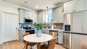 Una cocina moderna con armarios blancos, electrodomésticos de acero inoxidable y una mesa de comedor redonda con sillas.