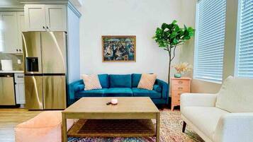 A living room with a blue sofa, a white sofa, a coffee table, and a kitchen area with a refrigerator.