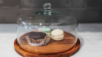 A dessert display with a glass dome over three macarons on a wooden board.