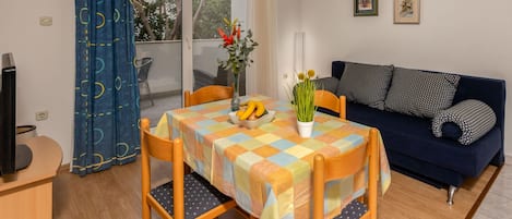 A room with a dining table, chairs, a sofa, and a TV.