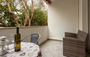 Un balcon avec une table, une chaise en osier et une bouteille de vin.