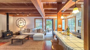 A cozy living room with a fireplace, a large clock, and a dining area with stools and a table. - Guerneville~Hot Tub~Fenced Yard~Dog Friendly~Russian River~Cabin~Fern Woods (Guerneville)