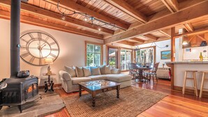 A cozy living room with a fireplace, a large clock, and a dining area with a view of the outdoors. - Guerneville~Hot Tub~Fenced Yard~Dog Friendly~Russian River~Cabin~Fern Woods (Guerneville)