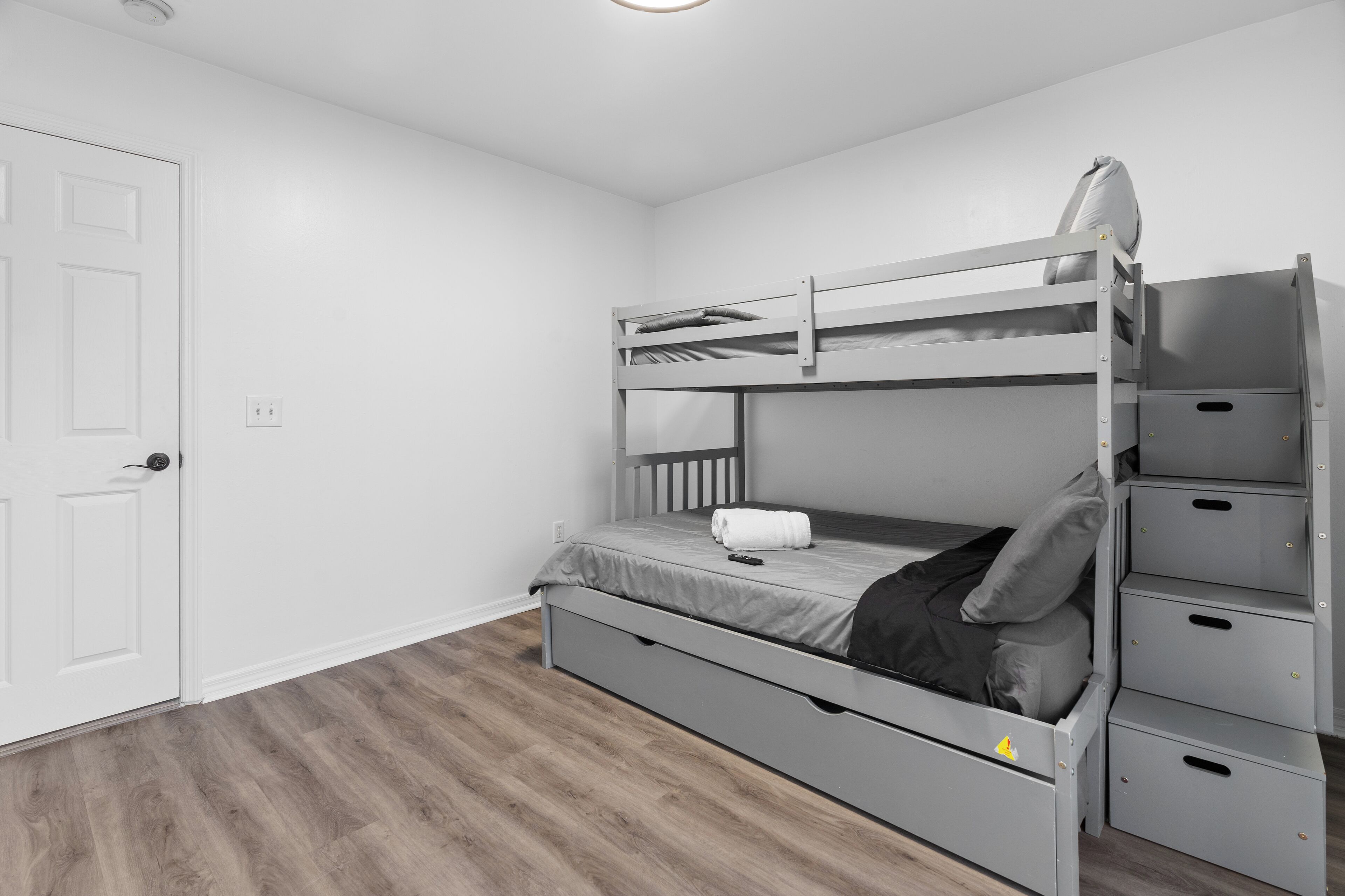 A bunk bed with storage drawers, a white door, and a wooden floor.