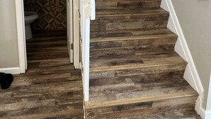 A staircase with wooden steps and white railings, leading to a room with a toilet and patterned wall tiles.
