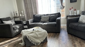 A modern living room with a grey sofa set, a white throw blanket, and a wooden floor.