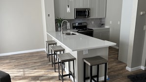 A modern kitchen with a central island, bar stools, stainless steel appliances, and a potted plant.