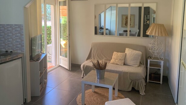 A compact living space with a kitchenette, a sofa, a coffee table, and a lamp. - Joli Studio rdc Avec Jardin Privé et Ombragé (LE CANNET DES MAURES)