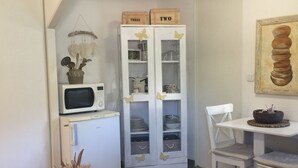 A compact kitchen with a microwave, a white cabinet with glass doors, a small table, and a chair. - Joli Studio rdc Avec Jardin Privé et Ombragé (LE CANNET DES MAURES)