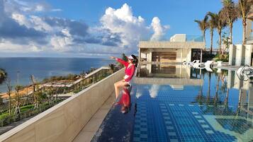 A person sitting on the edge of a pool with a view of the ocean and a modern building in the background.