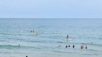 Une scène de plage où l’on voit des gens pagayer sur des planches de surf et nager dans l’océan.