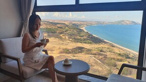 Una persona sentada junto a una ventana con vistas a un paisaje costero.