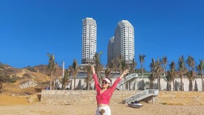 Una persona de pie en una playa arenosa con dos edificios altos al fondo.