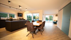 Een moderne keuken met een centraal eiland, een eethoek met een houten tafel en stoelen, en grote ramen met uitzicht op de omgeving.