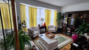 Een woonkamer met armstoelen met bloemenprint, een witte salontafel, een televisie en een boekenkast.