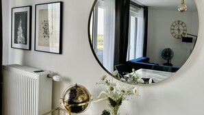 Una habitación con un espejo redondo grande que refleja un sofá azul, un globo terráqueo y un radiador. Hay dos cuadros en la pared.