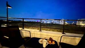 Un balcón con una mesa dispuesta para dos personas, una silla y vistas a la ciudad de noche.