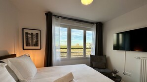 Una habitación de hotel con cama, una silla, un televisor y una ventana con vistas a la ciudad.