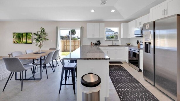 A modern kitchen with white cabinets, stainless steel appliances, and a dining area with a table and chairs. - 3 minute walk to the beach, outdoor shower, pet friendly, close to downtown (St. Augustine)