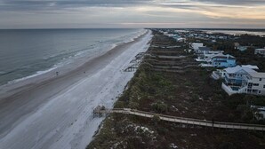 A beach with a wooden walkway leading to a white building with multiple stories and balconies. - 3 minute walk to the beach, outdoor shower, pet friendly, close to downtown (St. Augustine)