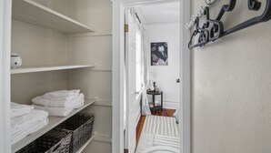 Un pasillo con una puerta blanca que da a una habitación, un perchero con varios ganchos y estantes con toallas dobladas.
