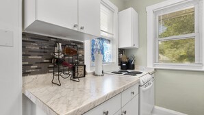 Una cocina con armarios blancos, encimera de mármol, estufa y ventana con persianas.