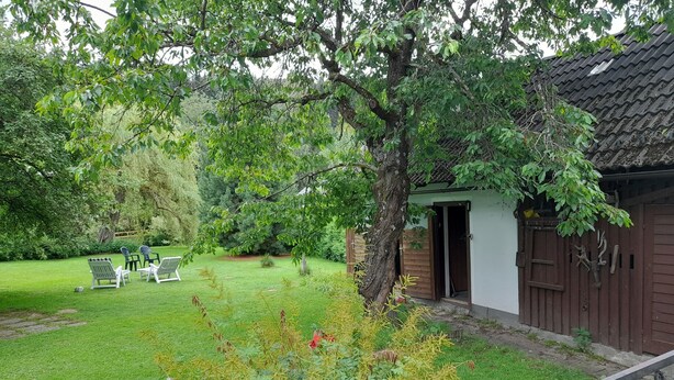 Un espacio al aire libre rústico con un edificio de madera, un césped y algunas sillas exteriores.