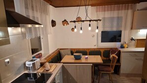 Una cocina compacta con horno integrado, tostadora y pileta. Hay una mesa de comedor de madera con sillas y una pequeña isla con un cuenco.