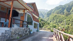 Un edificio moderno con balcón, pared de piedra y vistas a montañas verdes y exuberantes.