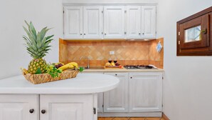 A kitchen with white cabinets, a white countertop, a stove, and a fruit basket with a pineapple and bananas. - Casa Maestrale 6, Emma Villas (Palau)
